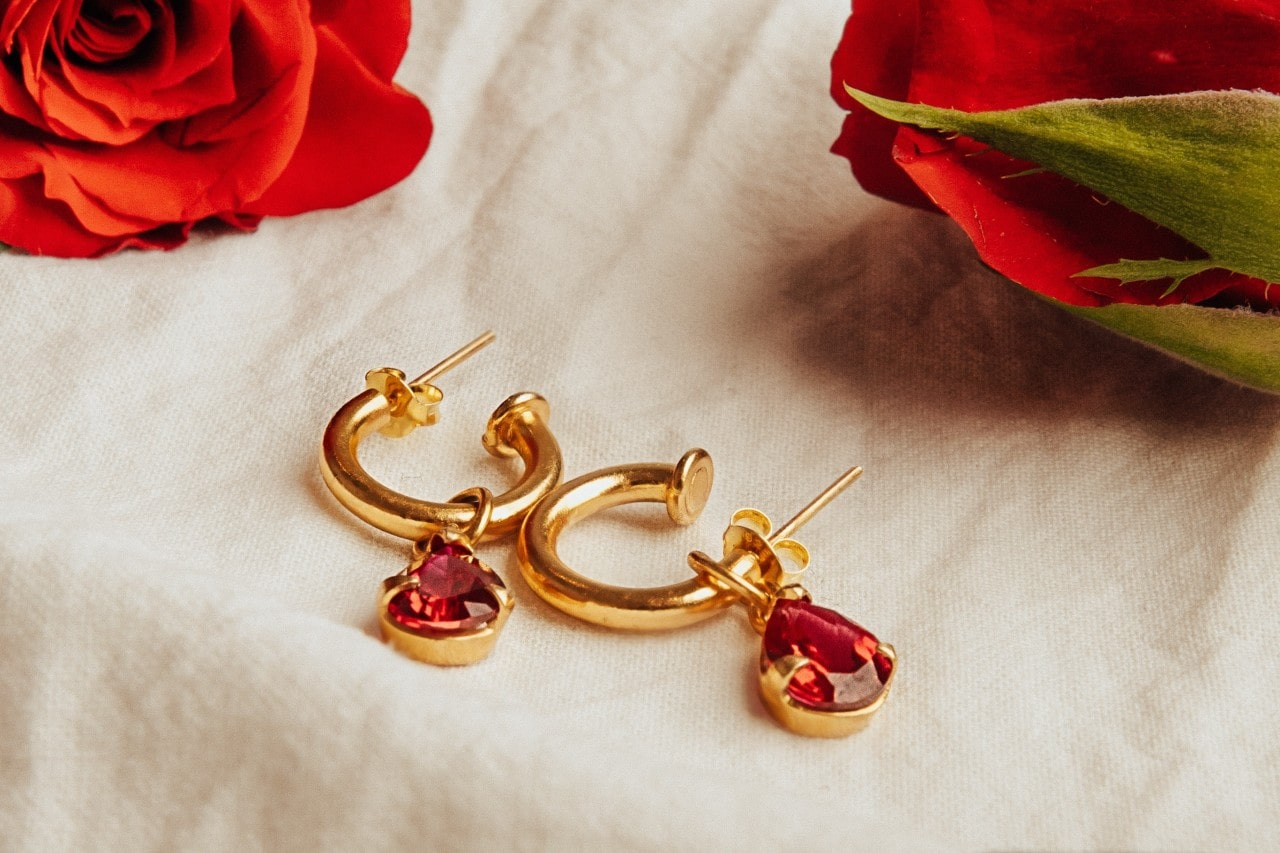  Pair of yellow gold mini hoops with ruby pendants on a piece of white linen