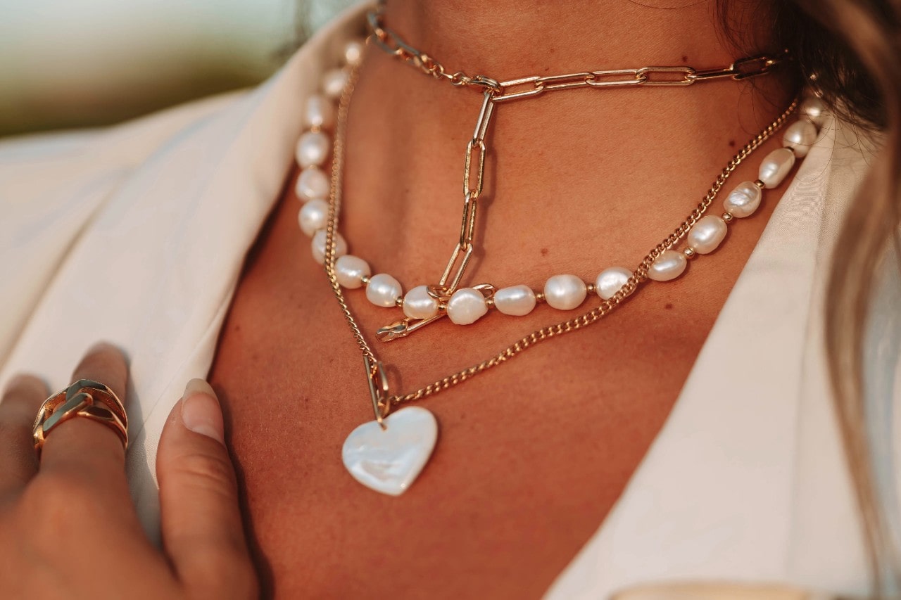A woman wearing three gold necklaces layered together, each with pearl accents