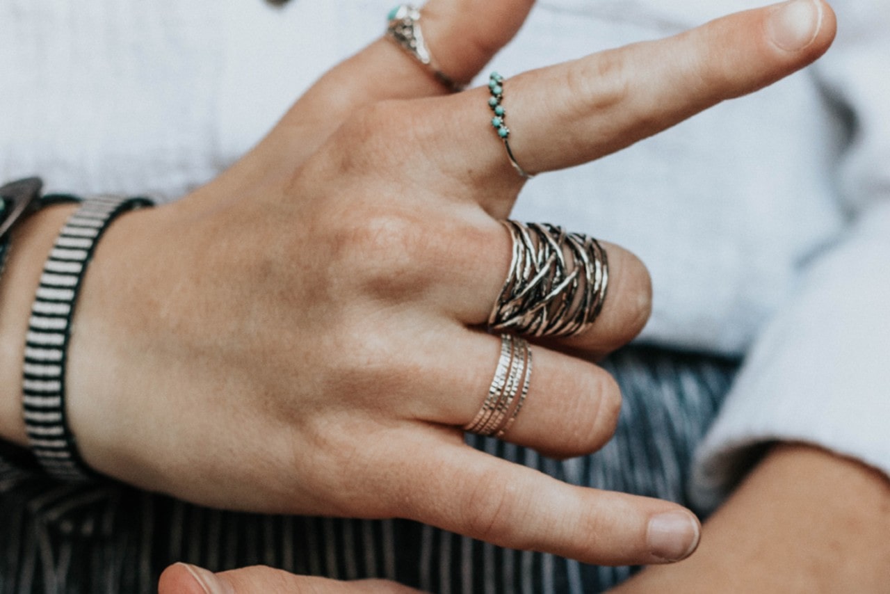 A hand wearing a silver bracelet and a number of stacked silver fashion rings