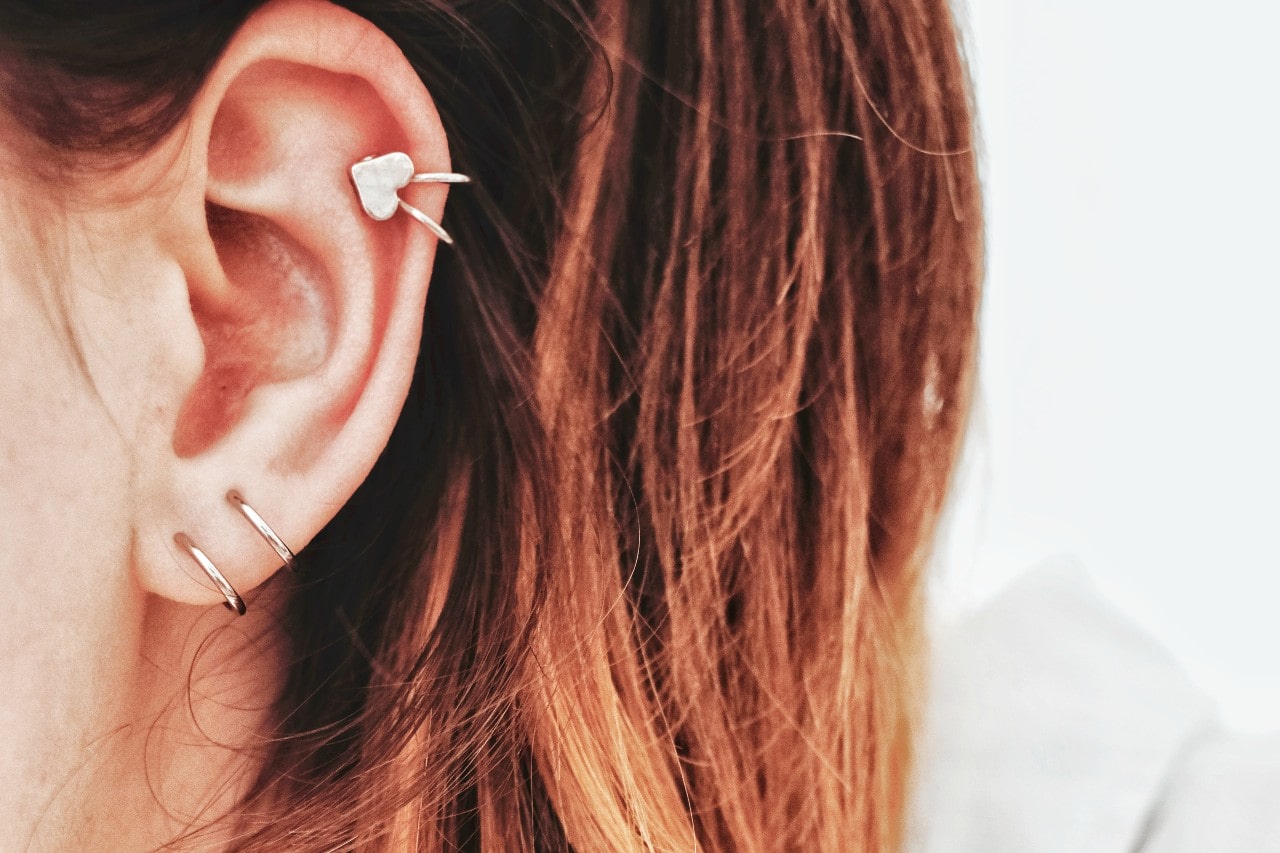 A woman’s ear wearing three gold huggies earrings