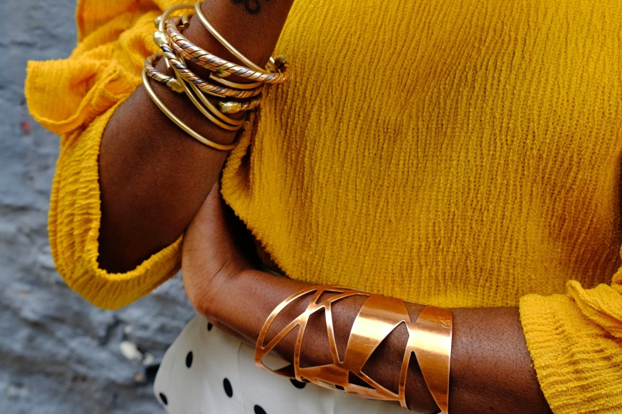 A woman in a yellow blouse wearing layers of gold bracelets