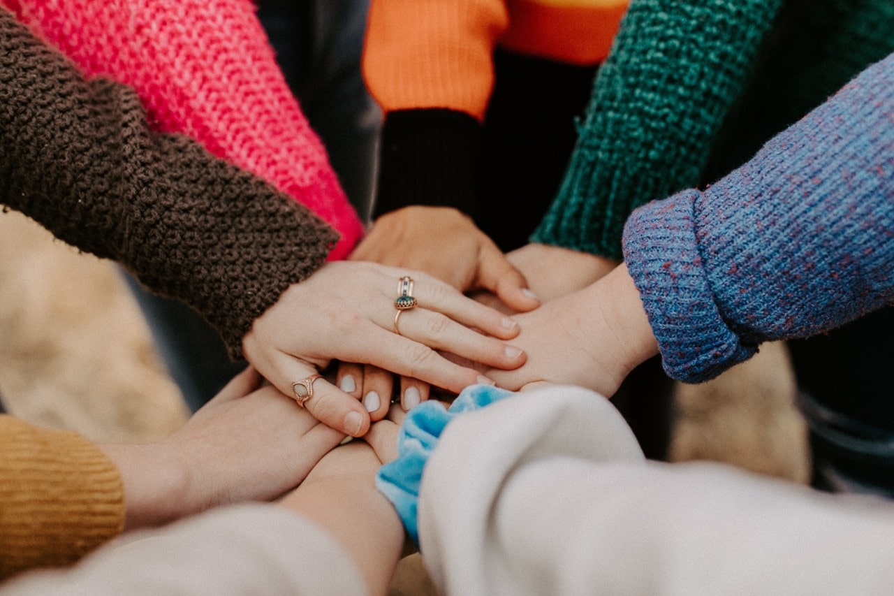 A group putting their hands together in celebration, all wearing fall sweaters and one wearing multiple yellow gold gemstone rings