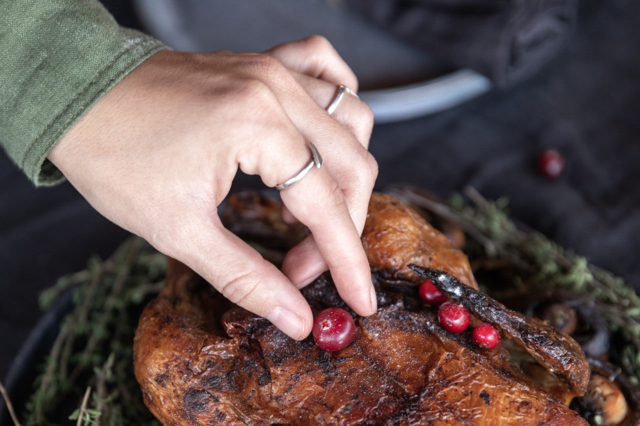 A woman wearing fashion rings places a cranberry on the Thanksgiving turkey.