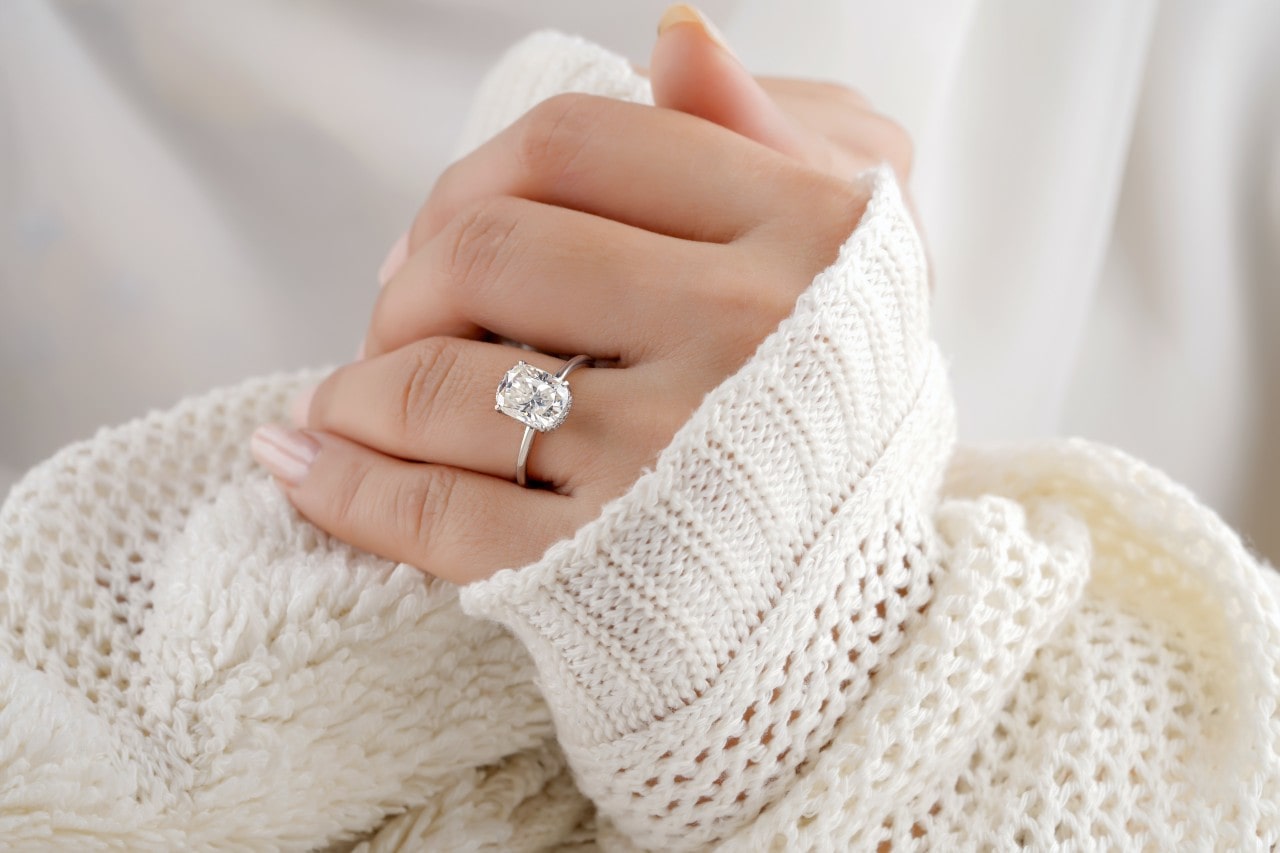 A woman in a white cashmere sweater shows off her oval cut engagement ring.