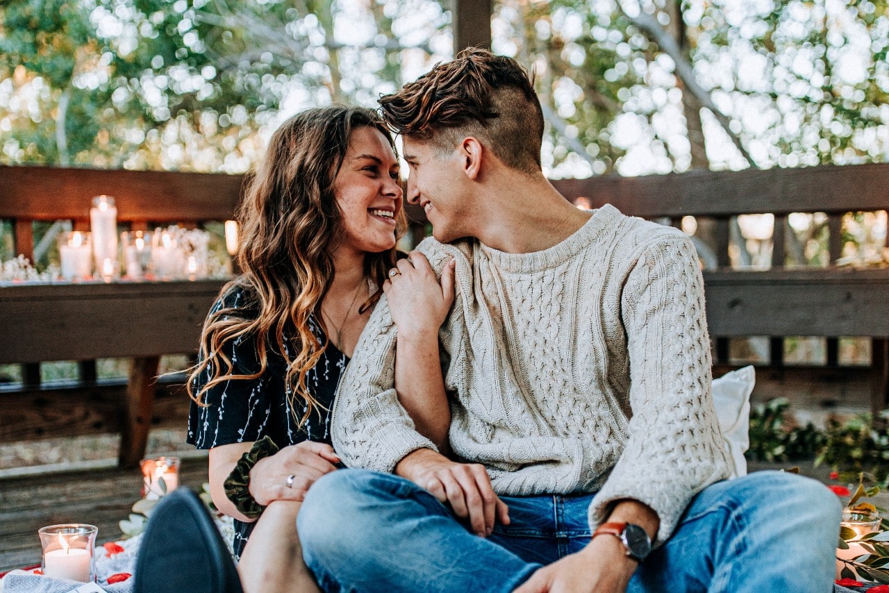 A happy couple sitting outside in a rustic yet cosy area, surrounded by candles.