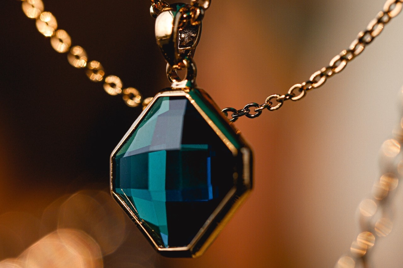 close up image of a yellow gold pendant necklace with a deep teal stone