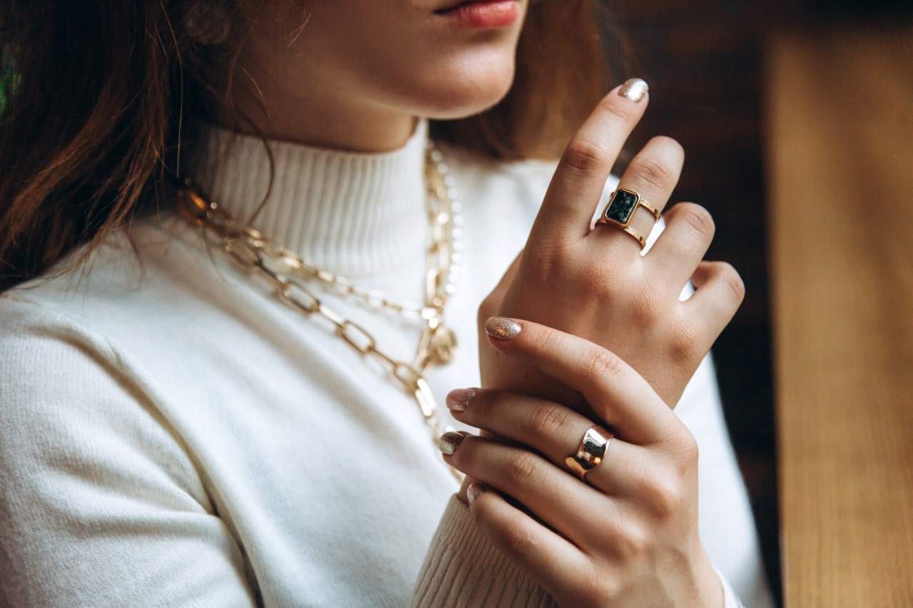 a woman looking out a window and showing off her yellow gold accessories