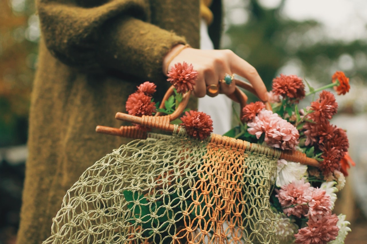 a woman holding a basket full of fall-toned flowers and wearing bold fashion rings