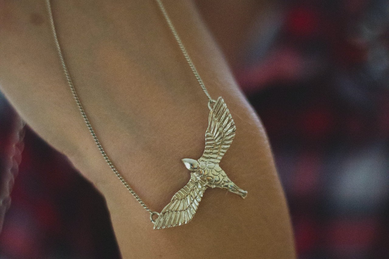 a person’s hand holding a yellow gold necklace with an eagle pendant