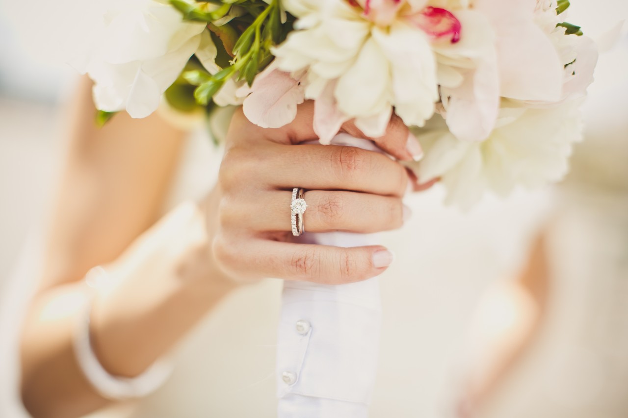 A close-up of a bride’s hand, holding a vibrant bouquet of summer flowers.