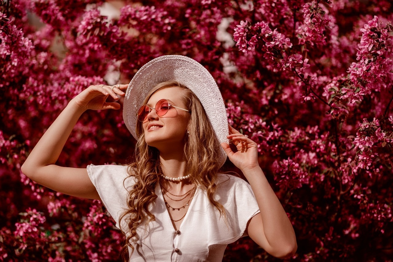 A pretty young woman posing in front of stunning pink flowers.