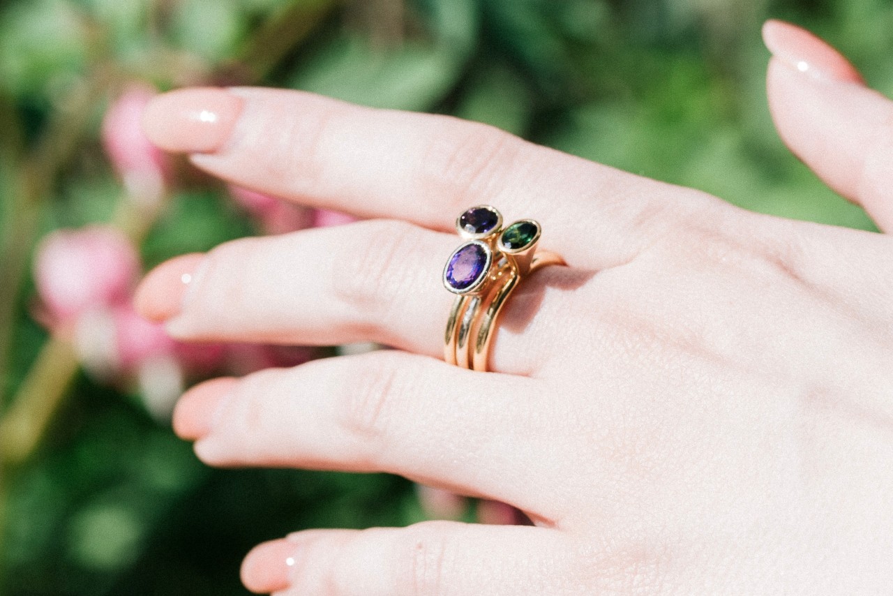 a woman’s outstretched hand wearing a stack of gemstone fashion rings