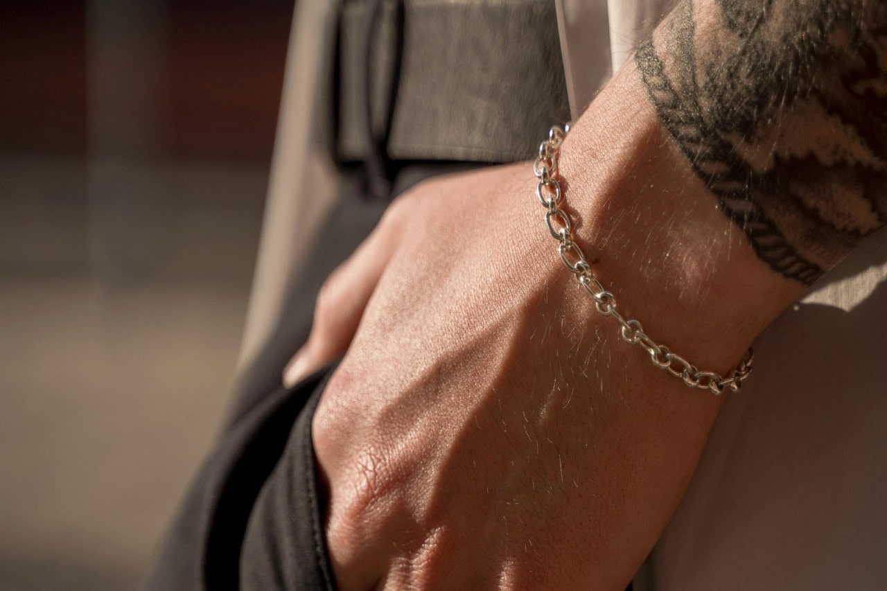 A close-up of a tattooed man’s wrist, adorned with a gold chain bracelet.