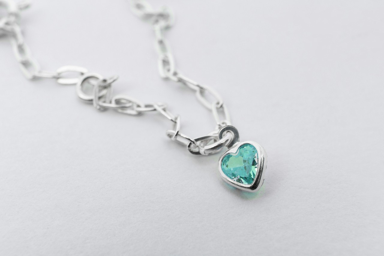 A close-up of a delicate necklace with a heart-shaped blue topaz pendant.