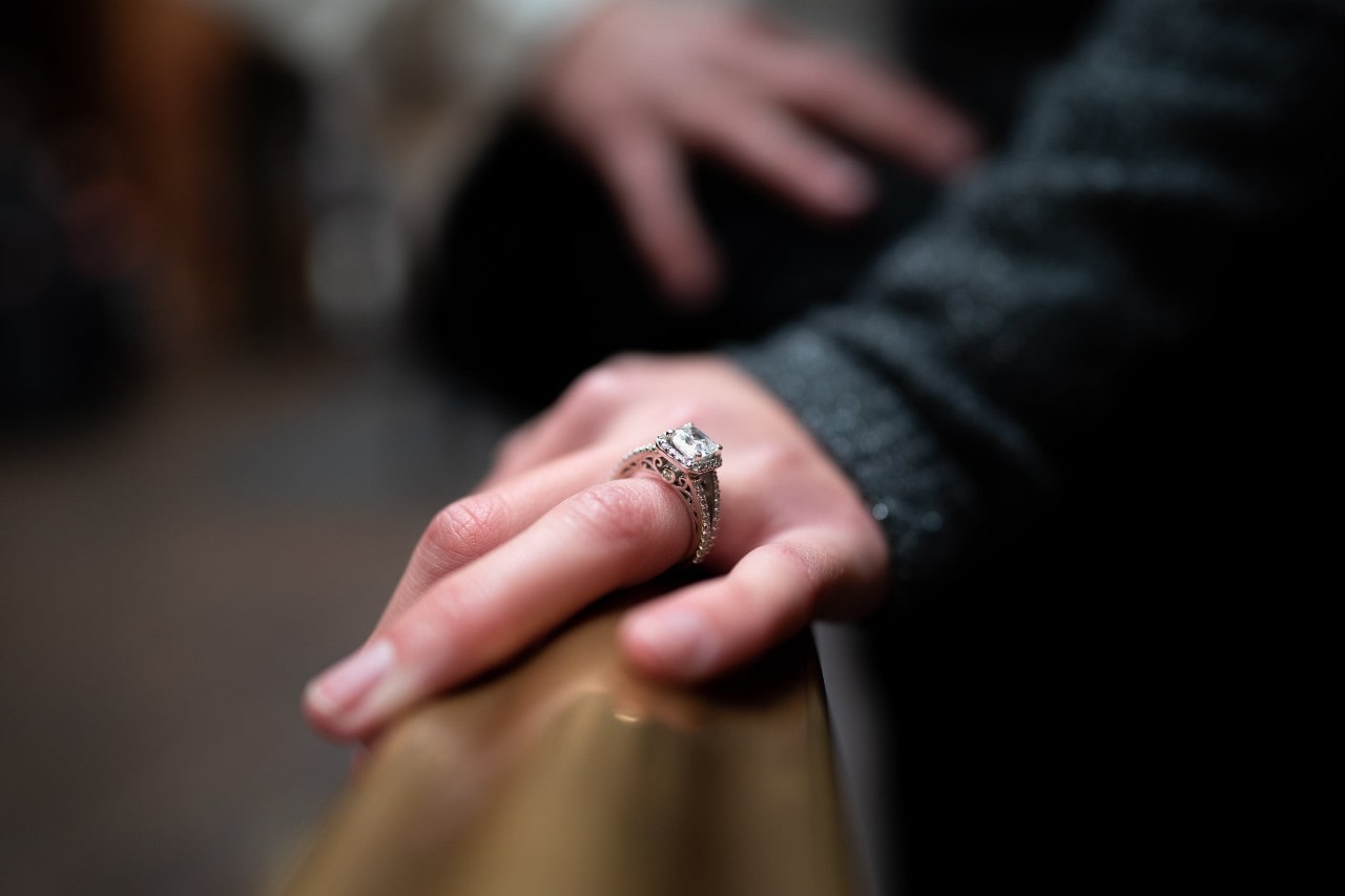 a hand on a bannister wearing an elaborate halo engagement ring