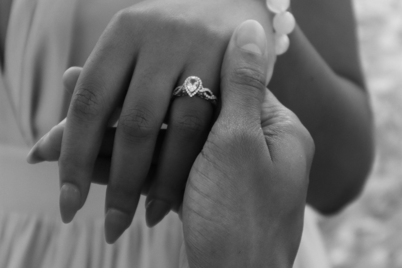 a man’s hand holding a lady’s hand that’s wearing a pear-shaped engagement ring