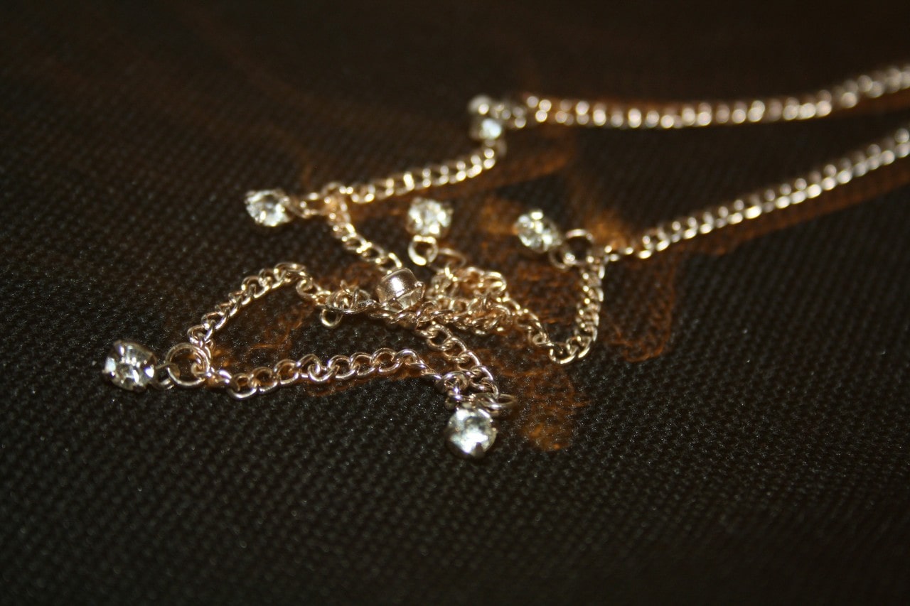 A close-up of a gold station necklace on a dark textured backdrop.