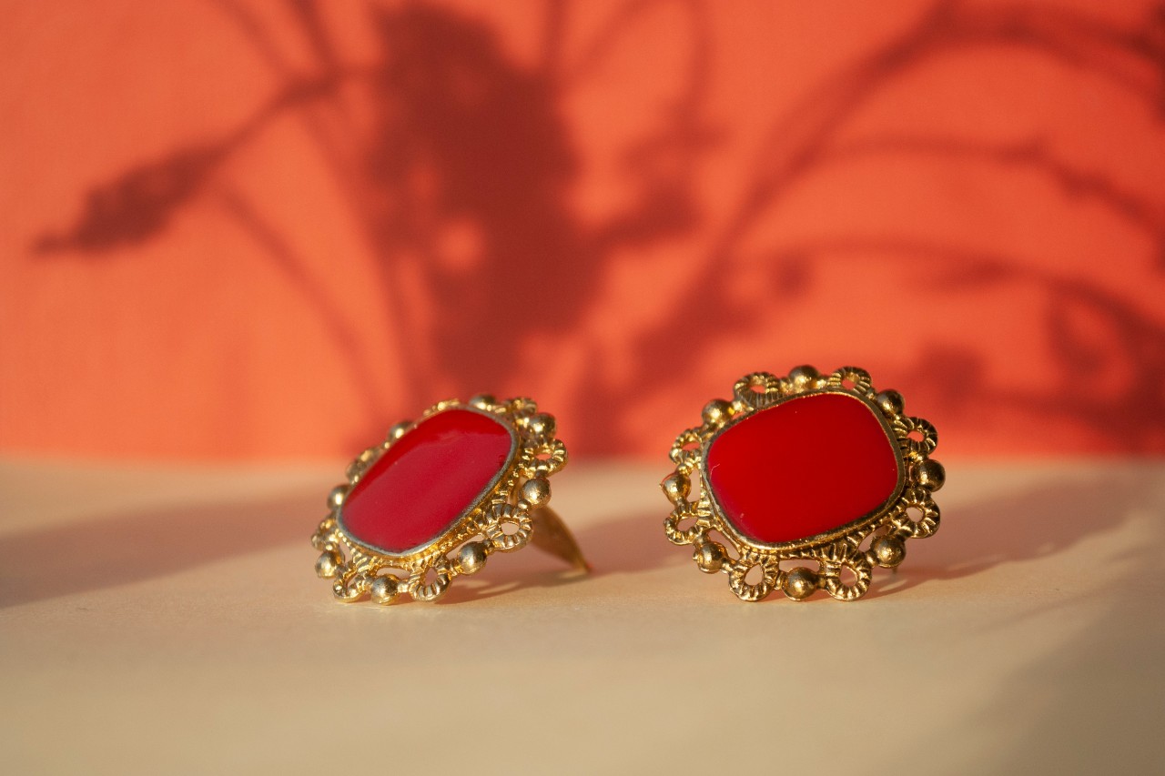 A close-up of ornate gold earrings on a vibrant background.